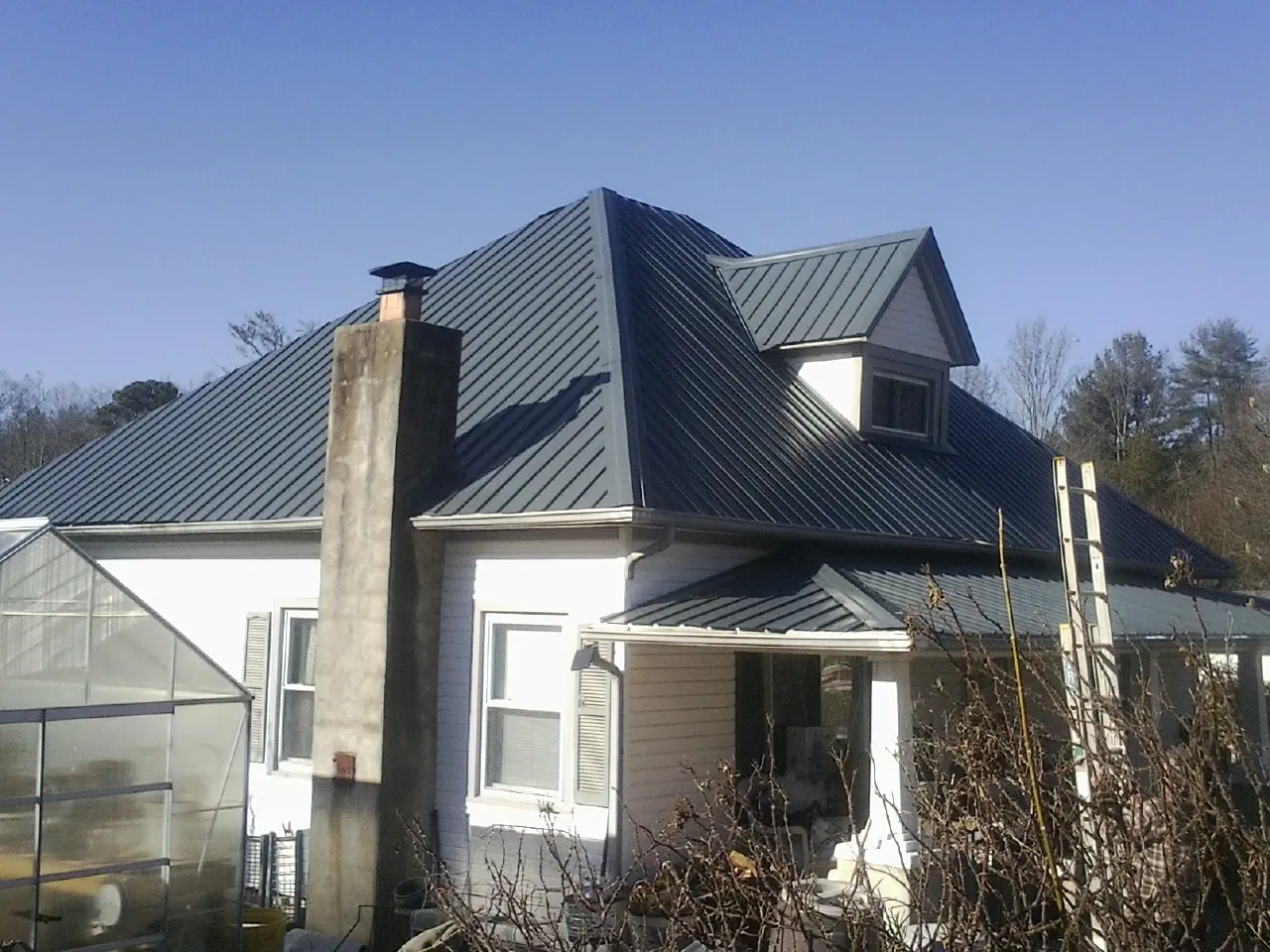 Dark blue standing seam metal roof on a white farmhouse with dormer — Slate & Tile Roof Repair by Roofing Brothers in Gunlock