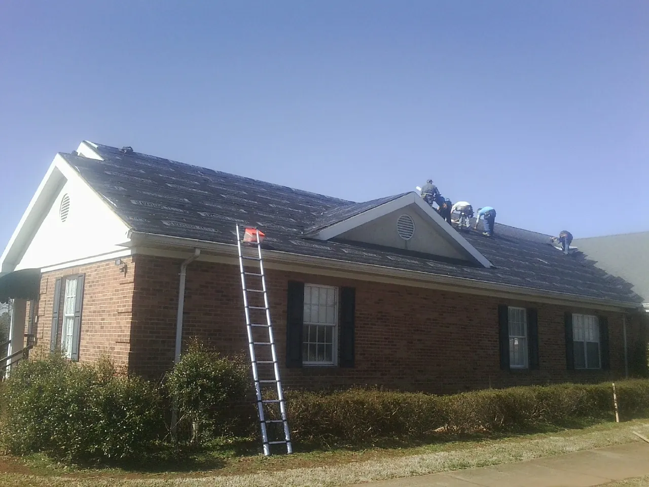Crew tearing shingles off a brick ranch roof with a ladder set — Emergency Roof Repair work by our crew in Gunlock