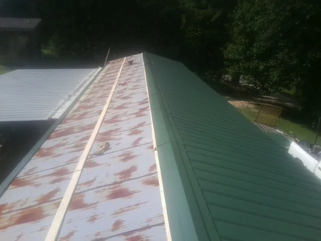 Old rusted panels beside newly installed green metal roofing — Wind Damage Roof Repair by Roofing Brothers in Gunlock