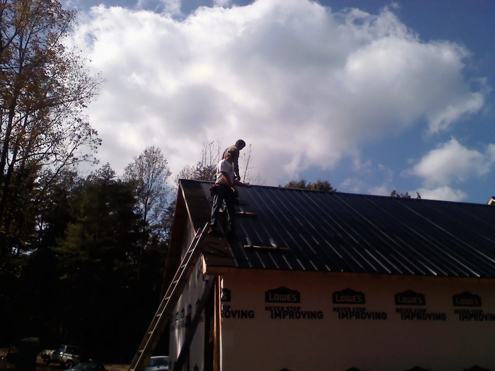 Roofer fastening dark metal panels high against a cloudy sky, from a Roof Inspection job in Gunlock