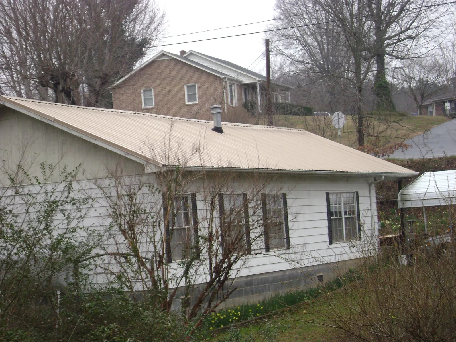 Tan metal roof on a white sided house set into a hillside — Commercial Roofing by Roofing Brothers in Gunlock
